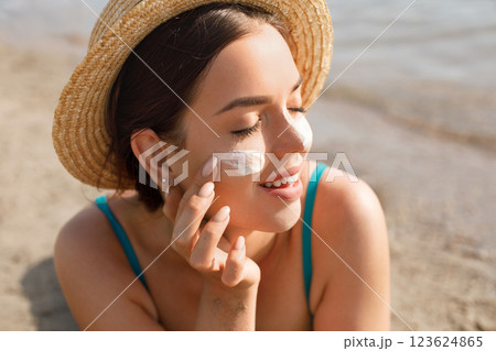 Beautiful Young woman with sun cream on face.  Female in hat applying moisturizing lotion on skin.Skin care. Sun protection. Suntan 123624865
