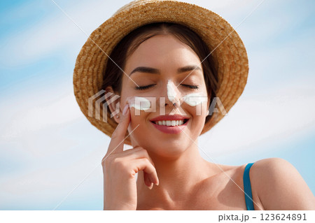 Woman smile applying sun cream on face. Skincare. Body Sun protection. sunscreen. Female in hat smear moisturizing lotion on skin. 123624891