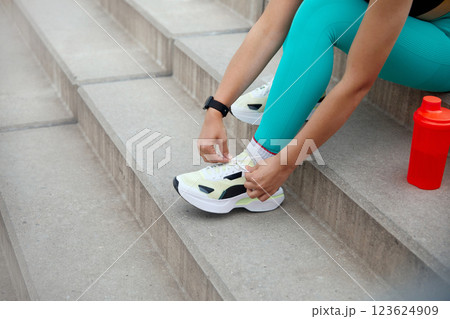 Fitness Enthusiast Ties Shoelaces While Preparing for Workout on Outdoor Stairs in Bright Athletic Gear 123624909