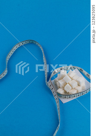 Sugar cubes and measuring tape on a blue background showcasing health awareness Sugar cubes and measuring tape on a blue background showcasing health awareness 123625095