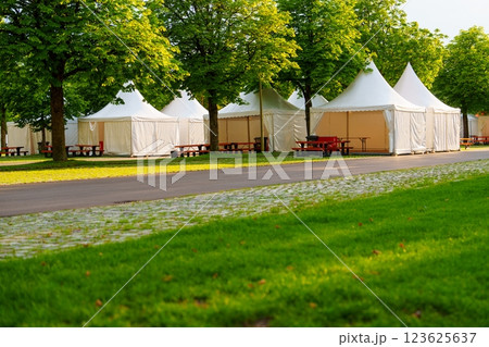 Stunning white party tents elegantly arranged in a beautiful park setting surrounded by greenery. Stunning white party tents elegantly arranged in a beautiful park setting surrounded by greenery. 123625637