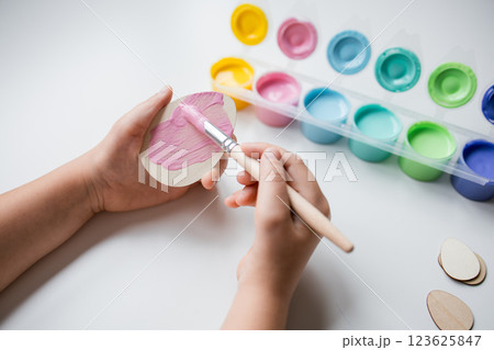 Child painting Easter wooden egg using pink acrylic paint on white surface 123625847