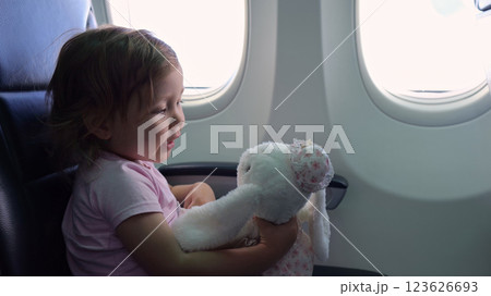 Cute blonde child hugs toy bunny sitting in airplane seat 123626693