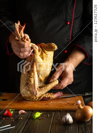 A chef skillfully handles a whole duck, preparing it for cooking on a wooden cutting board in a kitchen. Fresh ingredients like garlic and onion are nearby 123627326