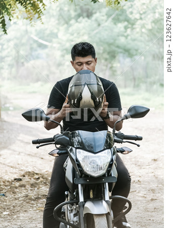 Man on motorcycle putting on helmet, motorcyclist putting on safety helmet, person on motorcycle putting on safety helmet 123627642