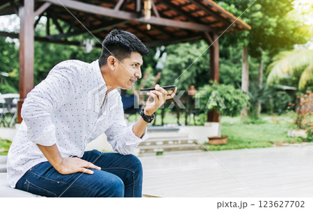 Handsome man sitting outside sending a voice message with his cell phone, Teenage sitting calling on the phone outside, Attractive man sitting sending a voice message with his phone and gesturing Handsome man sitting outside sending a voice message with his cell phone, Teenage sitting calling on the phone outside, Attractive man sitting sending a voice message with his phone and gesturing 123627702