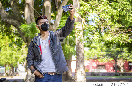 young man with mask taking a selfie, young man taking a selfie, man in jacket and mask taking a selfie 123627704