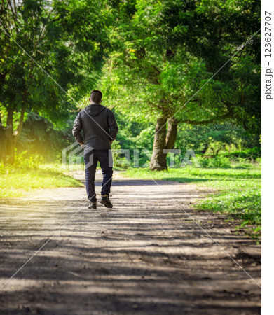 Man walking down a desolate road, man walking backwards on a road surrounded by vegetation Man walking down a desolate road, man walking backwards on a road surrounded by vegetation 123627707