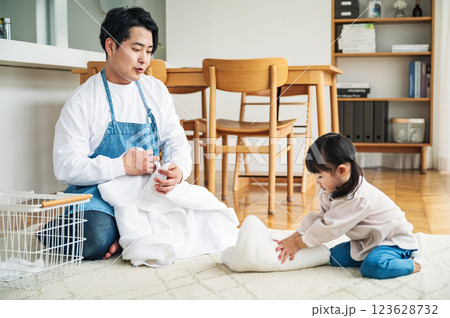 パパと一緒に洗濯物を畳むのを手伝う幼い娘 パパと一緒に洗濯物を畳むのを手伝う幼い娘 123628732