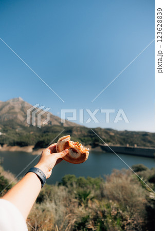 Hand holding bagel with mountain and lake view under clear blue sky Hand holding bagel with mountain and lake view under clear blue sky 123628839