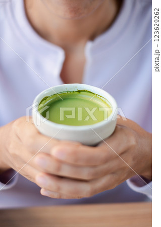 A person holding a cup of vibrant green matcha tea, capturing a moment of relaxation and warmth. A person holding a cup of vibrant green matcha tea, capturing a moment of relaxation and warmth. 123629262
