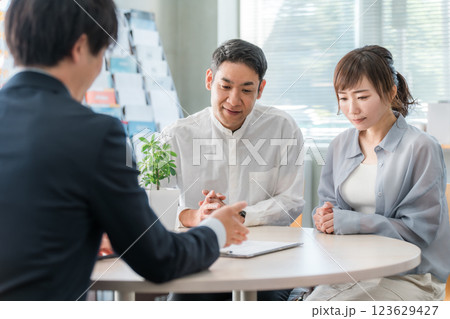 ショールーム・商談スペースで話を聞く夫婦と接客するビジネスマン 123629427