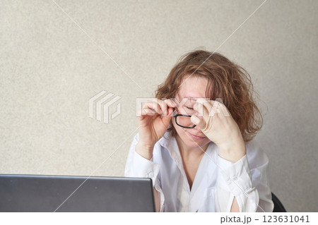 Caucasian mature female struggling with eyeglasses at laptop in office setting Caucasian mature female struggling with eyeglasses at laptop in office setting 123631041