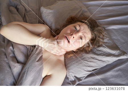 Caucasian adult female with sore throat lying in bed holding neck and looking 123631078