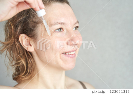 Caucasian adult female applying facial serum for skincare with dropper 123631315