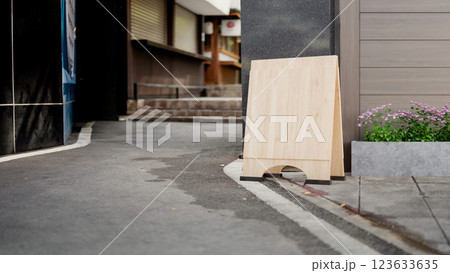 The blank wooden signboard places on the concrete sidewalk in front of the market or avenue entrance 123633635