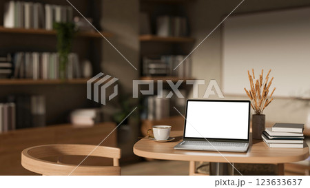 The white screen laptop place between a cup and books on a round wooden table in the dim light room The white screen laptop place between a cup and books on a round wooden table in the dim light room 123633637