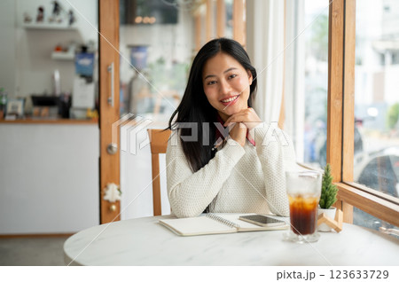 An asian woman is smiling while looking straight into the camera, sitting with a cold drink in cafe. 123633729