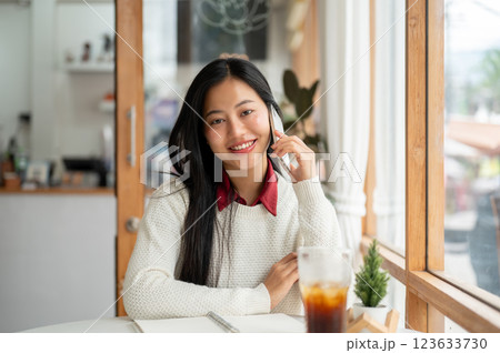 An asian woman is smiling during phone call while looking straight into the camera. sitting in cafe. 123633730