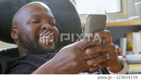 Front view of African american man using mobile phone in a comfortable home Front view of African american man using mobile phone in a comfortable home 123634139