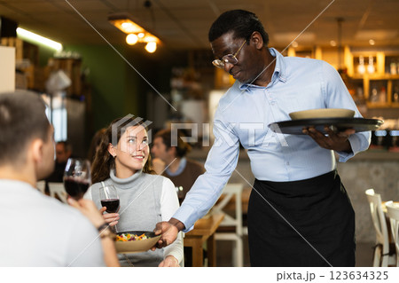 African man waiter serves cafe establishments girl visitor, puts food on table. African man waiter serves cafe establishments girl visitor, puts food on table. 123634325