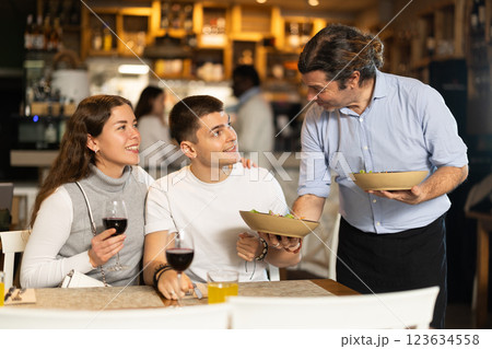 Male waiter brings dishes that the couple ordered Male waiter brings dishes that the couple ordered 123634558