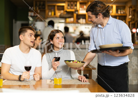 Man waiter serves cafe establishments couple visitor, puts food on table. Man waiter serves cafe establishments couple visitor, puts food on table. 123634828