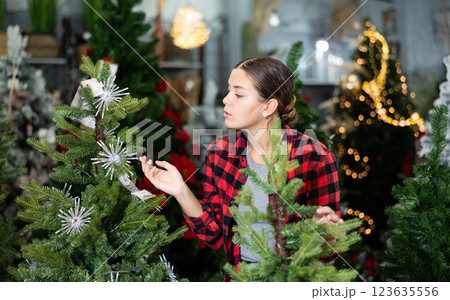 Smiling casual woman checking the material while standing near a Christmas tree in a shopping mall Smiling casual woman checking the material while standing near a Christmas tree in a shopping mall 123635556