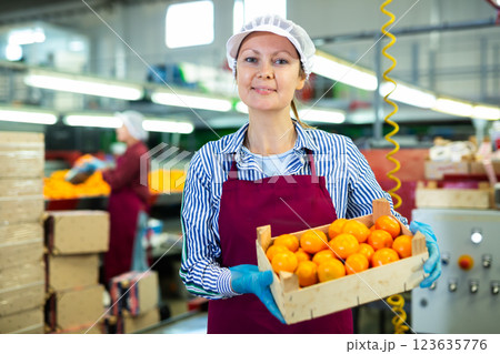 Positive female worker with box of mandarins at fruit sorting factory 123635776