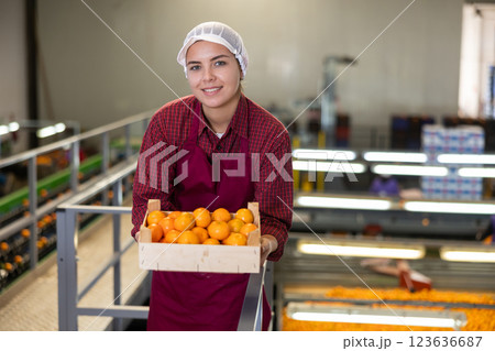Glad positive female employee in colored uniforms hold a box of fresh ripe tangerines in their hands on citrus sorting line at warehouse. 123636687