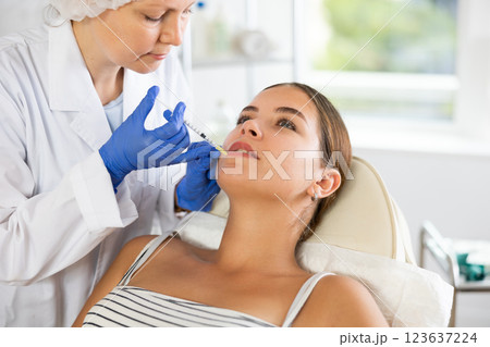 Adult woman cosmetologist makes injection in lips of patient Adult woman cosmetologist makes injection in lips of patient 123637224