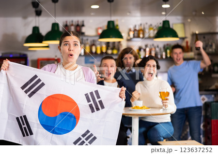Excited young adult sports fans rooting for favorite team and waving flag of South Korea while watching match together in pub Excited young adult sports fans rooting for favorite team and waving flag of South Korea while watching match together in pub 123637252