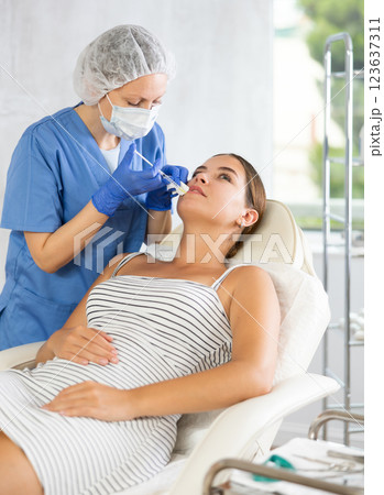 Adult woman cosmetologist makes injection in lips of patient 123637311