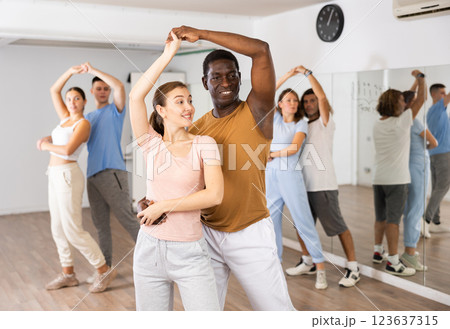 Positive smiling dancing couple enjoying active dancing during group training in dance hall Positive smiling dancing couple enjoying active dancing during group training in dance hall 123637315