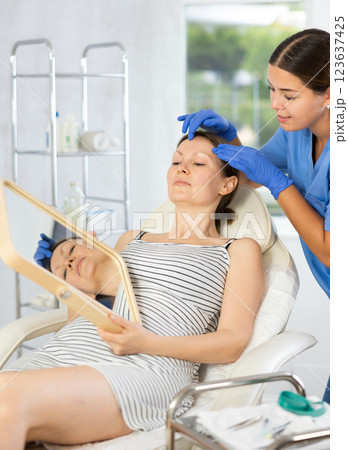 Young woman cosmetologists examines face of female patient Young woman cosmetologists examines face of female patient 123637425