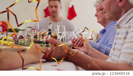 Image of stars over caucasian family with santa hats praying before christmas dinner Image of stars over caucasian family with santa hats praying before christmas dinner 123640516