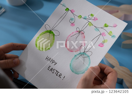 Person holding handmade greeting card with message HAPPY EASTER written in beautiful handwriting. Gesture shows excitement and joy for the upcoming event. Springtime holiday gift present zero cost 123642105