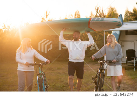 Friends enjoy a sunset adventure by the lake with bicycles and a paddleboard during an outdoor gathering Friends enjoy a sunset adventure by the lake with bicycles and a paddleboard during an outdoor gathering 123642274