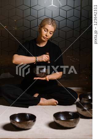 Practitioner uses singing bowls for meditation in a serene studio environment during a mindful evening session Practitioner uses singing bowls for meditation in a serene studio environment during a mindful evening session 123642311
