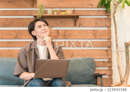 カフェ・喫茶店のソファでノートパソコンを使う若いアジア人男性 カフェ・喫茶店のソファでノートパソコンを使う若いアジア人男性 123642386
