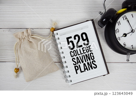 529 College Saving Plans text on notepad with money bag and alarm clock on wooden background 123643049