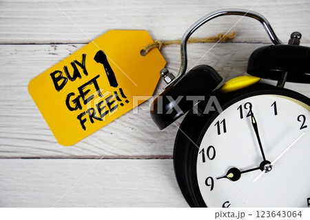 Buy 1 Get 1 Free!!! text on price tag with alarm clock on wooden background Buy 1 Get 1 Free!!! text on price tag with alarm clock on wooden background 123643064