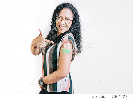 Smiling woman pointing at her vaccinated arm. Latin woman pointing at the bandage on her vaccinated arm 123644273