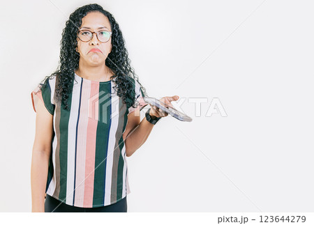 Indifferent girl holding cell phone isolated. Young skeptical woman with cell phone in hand isolated. Sad woman with cell phone looking at camera 123644279