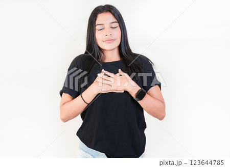 Thankful people with hands on chest. Grateful teenage girl smiling with hands on chest isolated. Positive latin girl with hands on chest Thankful people with hands on chest. Grateful teenage girl smiling with hands on chest isolated. Positive latin girl with hands on chest 123644785