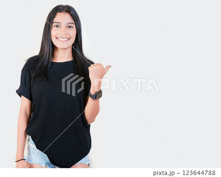 Friendly young girl pointing to a banner to the side. Happy latin woman recommending a promo isolated. Cheerful latin girl pointing an offer isolated Friendly young girl pointing to a banner to the side. Happy latin woman recommending a promo isolated. Cheerful latin girl pointing an offer isolated 123644788
