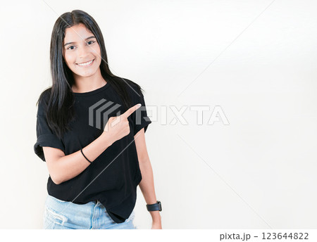 Smiling teenage girl pointing side with hand. Cheerful latin girl pointing an offer isolated. Happy teenager pointing a promo isolated Smiling teenage girl pointing side with hand. Cheerful latin girl pointing an offer isolated. Happy teenager pointing a promo isolated 123644822