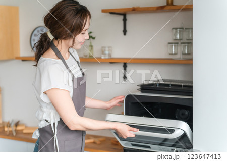 キッチンでキッチンで電子レンジを使う女性（笑顔） 123647413