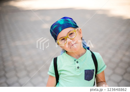 A funny little boy in glasses and a bandana, wearing a green t-shirt and denim shorts, having fun and joking A funny little boy in glasses and a bandana, wearing a green t-shirt and denim shorts, having fun and joking 123648862