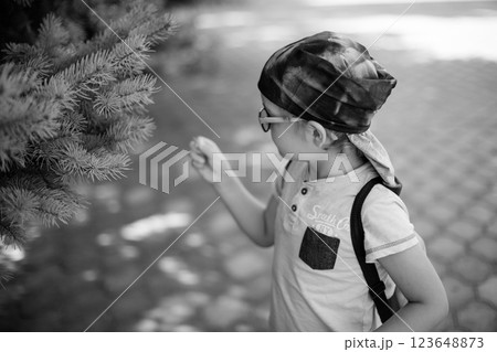 cute little boy in glasses and bandana, wearing green t-shirt, carefully studies plant while holding a toy monkey 123648873